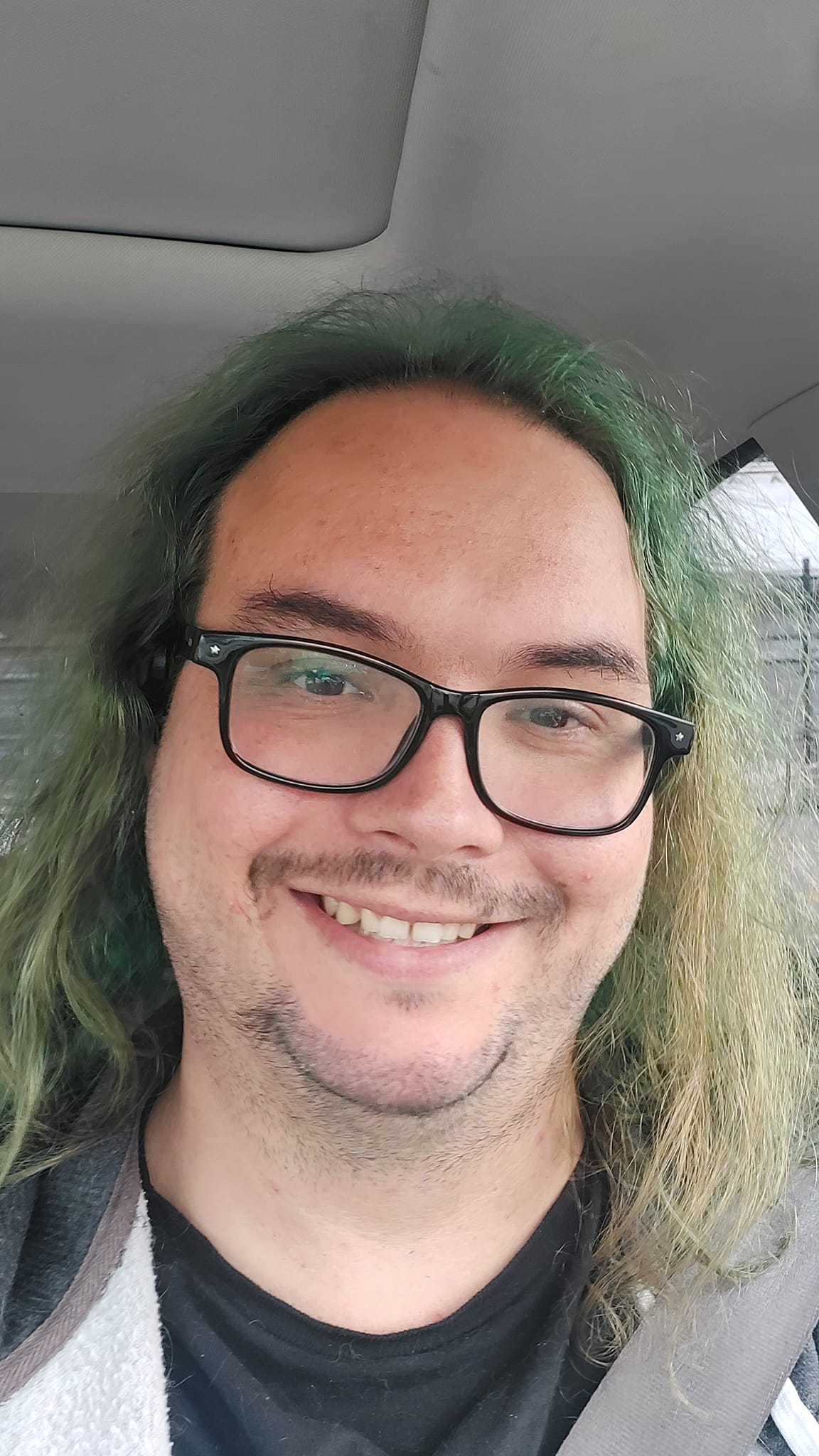 A man with long green hair and no beard sits in a car, Photo 3